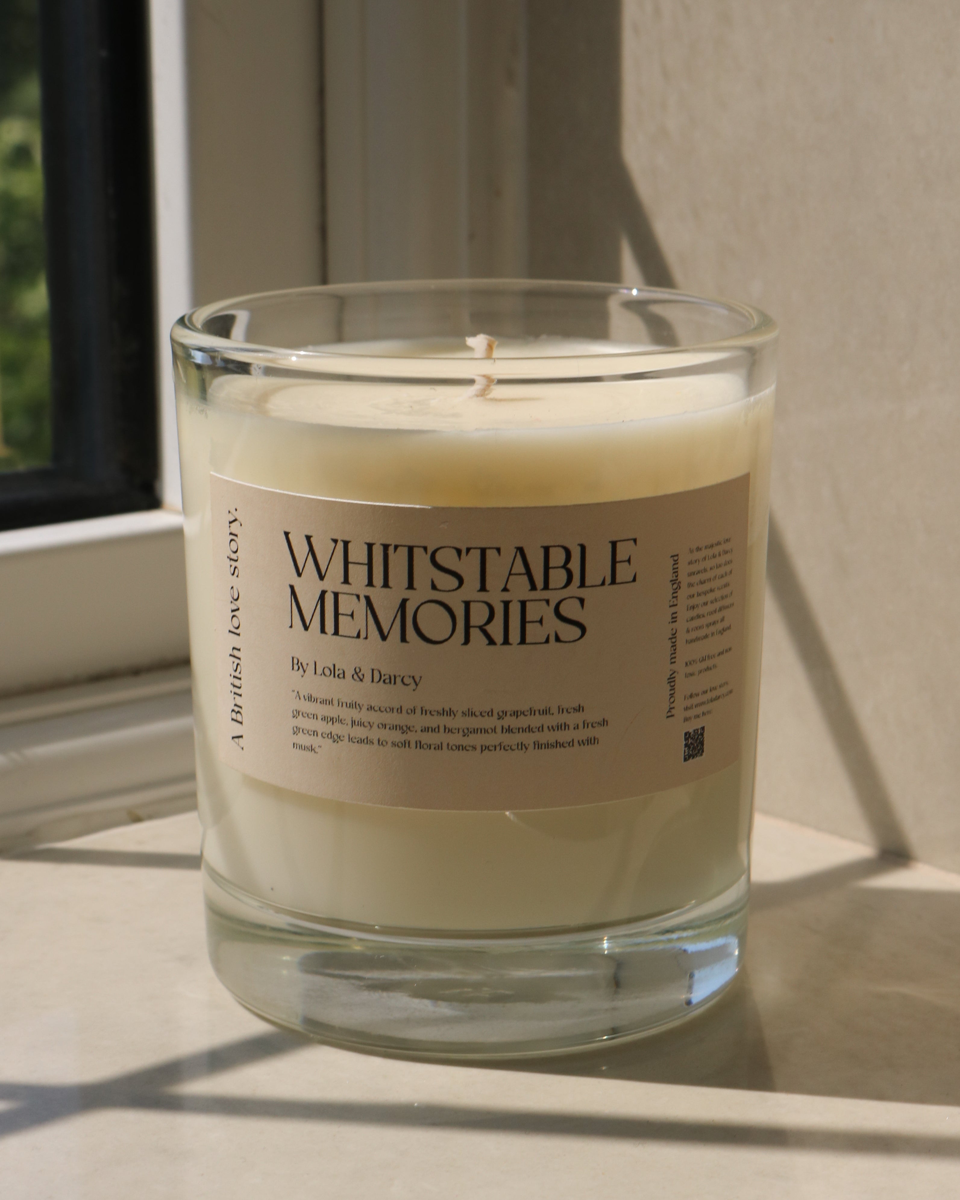 Candle in a glass jar labeled 'Whitstable Memories' on a windowsill.