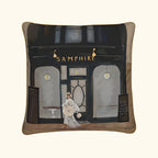 Pillow with a design of a woman walking past a store named 'Samphire' on a white background.Samphire Whitstable Luxury Cushion