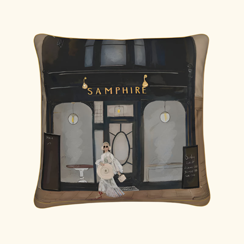 Pillow with a design of a woman walking past a store named 'Samphire' on a white background.Samphire Whitstable Luxury Cushion