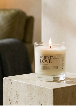 Candle labeled 'Whistable Love' on a stone surface with a blurred background of a cozy room.